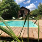 Piscine en bois, chaises longues, maison en brique, jardin luxuriant