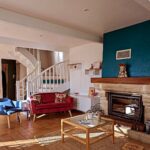 Salon avec canapé rouge, fauteuil bleu, cheminée et escalier blanc